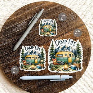 May include: Three vinyl stickers featuring a vintage camper van in a forest setting with the text "Camp Life". The stickers are available in 2 inch, 3 inch, and 4 inch sizes.