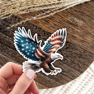 May include: A sticker of a bald eagle with its wings spread, featuring the American flag design. The eagle is flying with its talons extended.