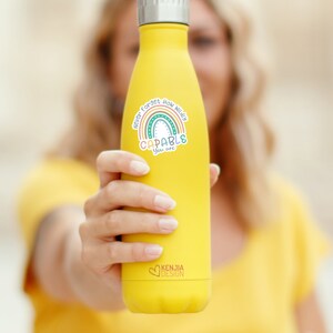 Op de afbeelding: Gele ge&iuml;soleerde waterfles met een zilveren deksel. De fles heeft een kleurrijke sticker met een regenboog en de woorden "Never Forget How Wildly Capable You Are". De fles heeft ook het logo "KENJIA DESIGN".
