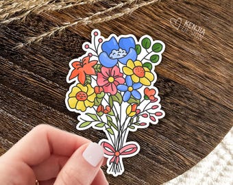 May include: A die-cut sticker featuring a colorful bouquet of illustrated flowers in shades of blue, yellow, pink, and orange, tied together with a pink ribbon bow. The sticker includes green leaves and stems, with the text KENJIA DESIGN printed in white.