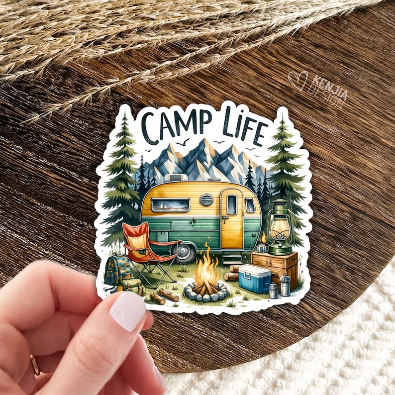 May include: A sticker featuring a vintage camper van parked in a forest setting with a campfire, a folding chair, and a lantern. The text "Camp Life" is written in a retro font above the camper.