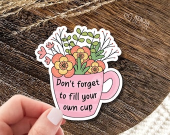 May include: A die-cut sticker featuring a pink mug with horizontal stripes, filled with a bouquet of orange, yellow, and green flowers. The text "Don't forget to fill your own cup" is printed in black on the front of the mug in a simple font.