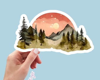 Puede incluir: Una pegatina troquelada con una ilustración de paisaje en acuarela de pinos verde oscuro y montañas grises sobre un cielo color melocotón suave con un sol amarillo pálido. El texto Kenjia design está impreso en una pequeña fuente cursiva blanca.