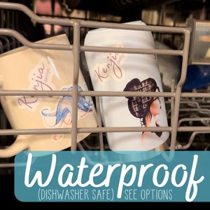 May include: Two white mugs with custom designs are in a dishwasher. The mugs are dishwasher safe and waterproof. The text on the mugs reads "Kenji design" and "Ryjia design".