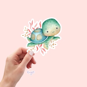 May include: A watercolor illustration of a green and blue sea turtle with a smiling face. The turtle is surrounded by pink and brown seaweed.