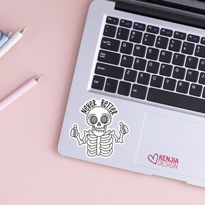 May include: A white sticker with a cartoon skeleton with a skull and crossbones. The skeleton is giving a thumbs up with both hands. The text "Never Better" is written in a circle around the skeleton.