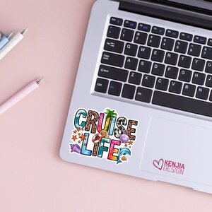 May include: A colorful sticker with the words "CRUISE LIFE" in a rainbow font. The sticker is decorated with various beach-themed elements, including seashells, starfish, palm trees, and a life preserver. The sticker is placed on a silver laptop.
