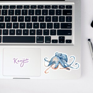 May include: A blue and orange watercolor octopus sticker with the text "Kenjia design" on a white background.