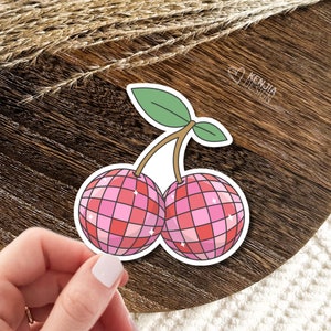 May include: A sticker of two pink cherries with a disco ball design. The cherries have a green stem and leaves.