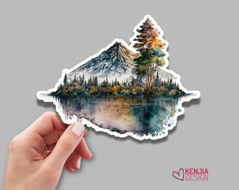 Puede incluir: Una pegatina troquelada con una ilustración en acuarela de una cordillera y un bosque reflejados en un lago tranquilo. La escena incluye un árbol alto prominente con follaje de tonos otoñales. El texto KENJIA DESIGN es visible.