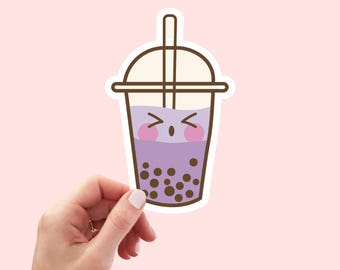 Puede incluir: Una pegatina troquelada que muestra un té de burbujas de dibujos animados en un vaso de plástico transparente con una pajita marrón. La bebida es de color violeta claro con perlas de tapioca oscuras y una cara con mejillas rosadas.