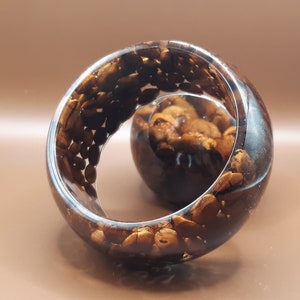 May include: A clear resin sculpture with a spiral design, filled with brown coffee beans. The sculpture has a glossy finish and is displayed on a brown surface. The coffee beans are visible throughout the sculpture.