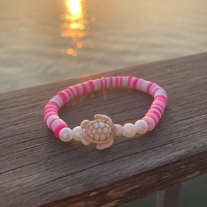 May include: A pink and white striped bracelet with a white turtle charm and white pearl beads.
