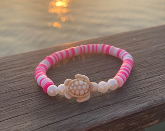 May include: A pink and white striped bracelet with a white turtle charm and white pearl beads.