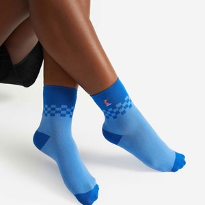 May include: Light blue socks with a checkered pattern on the cuff and a small orange fox logo. The socks have a solid blue toe and heel. The socks are made of a soft, comfortable material.