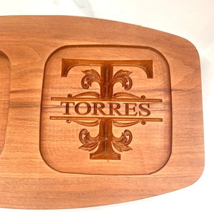 May include: A wooden serving tray featuring a carved design of the letter "T" with the name "TORRES" beneath. The tray has a natural wood finish and is ideal for serving snacks or appetizers.