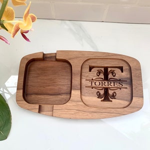 May include: A wooden tray with two compartments. The larger compartment features a decorative design with the letter "T" and the name "TORRES" engraved in it. The smaller compartment is empty.