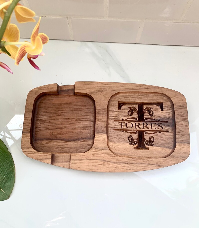May include: A wooden tray with two compartments. The larger compartment features a decorative design with the letter "T" and the name "TORRES" engraved in it. The smaller compartment is empty.