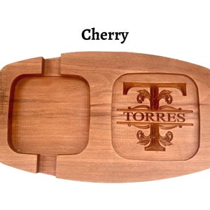 May include: A wooden serving tray with a square compartment and a round compartment. The round compartment has a personalised monogram with the letter "T" and the name "TORRES" engraved in it. The tray is made of cherry wood.