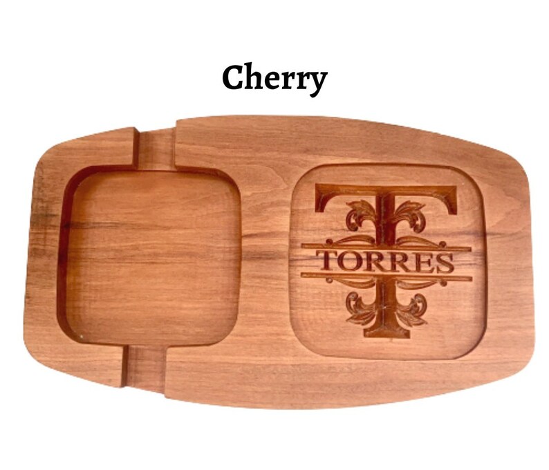May include: A wooden serving tray with a square compartment and a round compartment. The round compartment has a personalised monogram with the letter "T" and the name "TORRES" engraved in it. The tray is made of cherry wood.