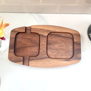 May include: A wooden serving tray with two separate compartments. The tray is made of dark brown wood and has a smooth, polished finish.