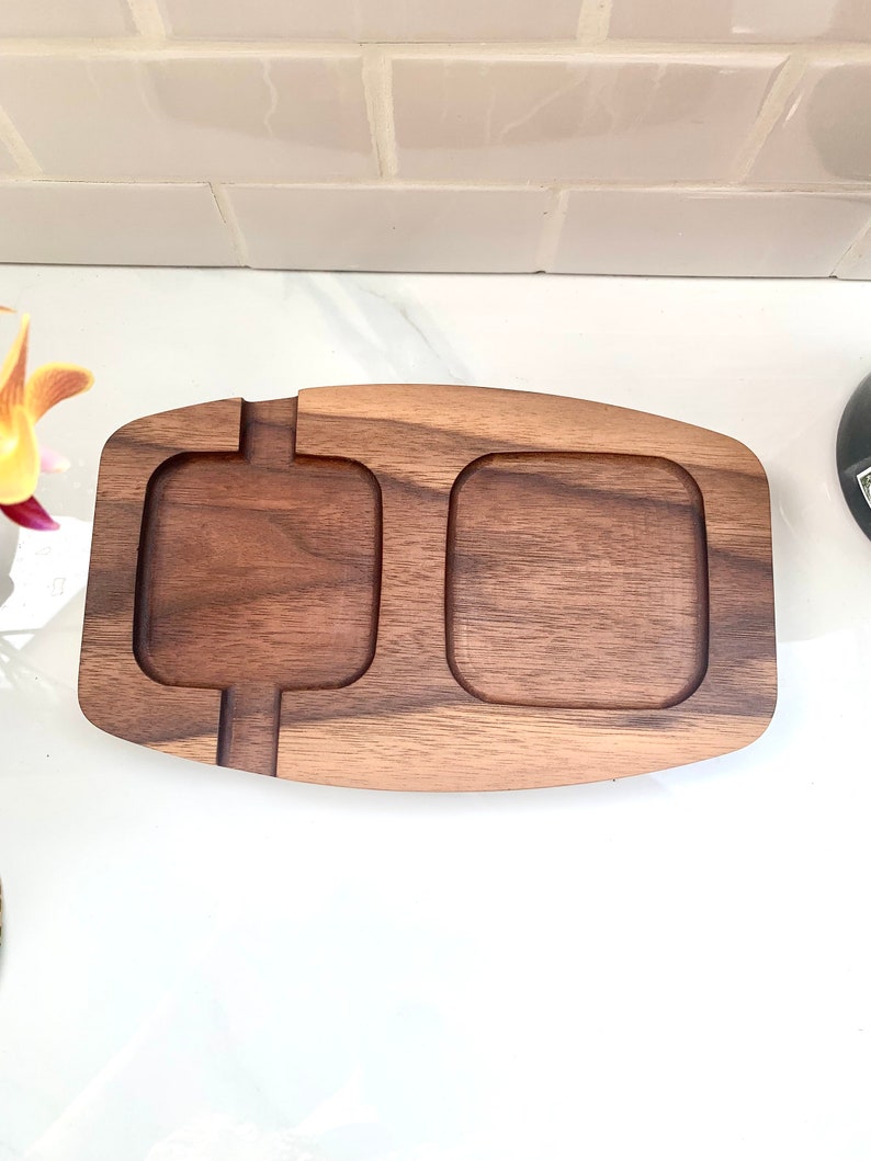 May include: A wooden serving tray with two separate compartments. The tray is made of dark brown wood and has a smooth, polished finish.