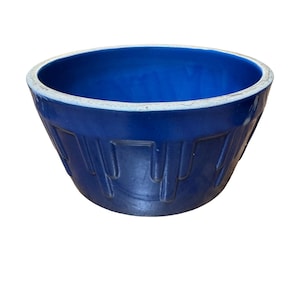 May include: A deep blue ceramic mixing bowl with a white rim. The bowl has a flared shape and vertical, grooved detailing on the exterior. This vintage kitchenware item is suitable for baking and food preparation.