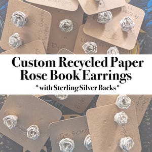 Puede incluir: Pendientes de rosas de papel reciclado personalizados con parte trasera de plata de ley. Los pendientes están hechos de papel enrollado, con forma de pequeñas rosas. Se muestran en pequeñas tarjetas marrones.