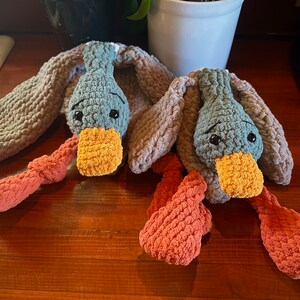 May include: Two crocheted plush duck toys with orange and gray bodies and blue heads. The ducks have orange beaks and black eyes.