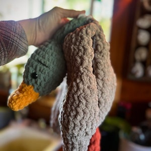 May include: A crocheted gray and orange goose toy with a long neck and a textured surface.