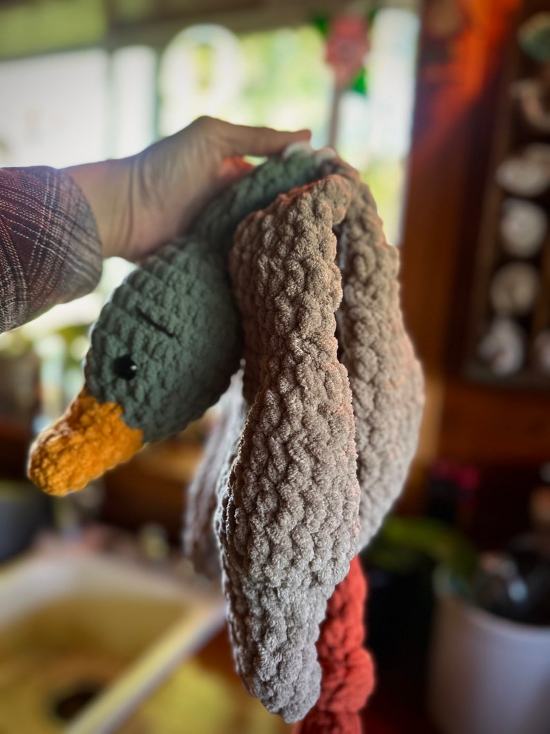 May include: A crocheted gray and orange goose toy with a long neck and a textured surface.