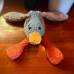 May include: A crocheted stuffed duck toy with brown, gray, and orange yarn. The duck has a long orange beak and black eyes.