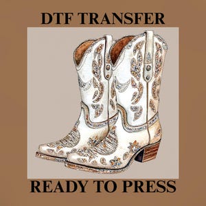 Pode incluir: Botas de cowboy brancas com intrincados padrões florais e geométricos, saltos castanhos e detalhes brilhantes. O texto "DTF TRANSFER" e "READY TO PRESS" está presente.
