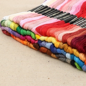 May include: A collection of colorful embroidery floss in a variety of shades, including pinks, reds, greens, blues, and yellows. The floss is neatly organized, with each color separated. The image shows a close-up view of the floss, highlighting the texture and vibrancy of the threads.
