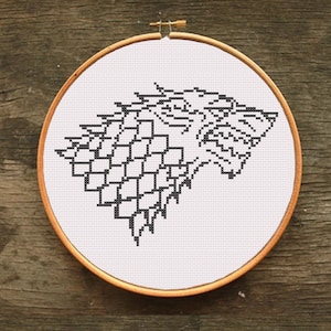 May include: A black and white embroidery design of a direwolf head, a popular symbol from the TV show Game of Thrones, in a circular embroidery hoop.
