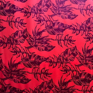 May include: Red fabric with a repeating pattern of dark purple tropical leaves and foliage. The leaves are large and detailed, creating a bold contrast against the bright red background. The design is likely suitable for apparel or home decor.