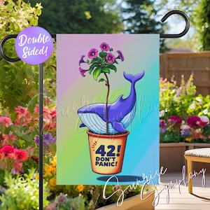 May include: A double-sided garden flag featuring a purple whale with a plant growing out of its back, set in a pot with the text "42! DON'T PANIC!". The flag has a colorful background and is displayed outdoors.