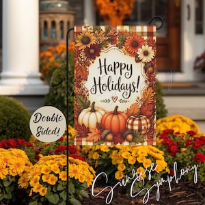 May include: A rectangular garden flag featuring a cream-coloured centre with the text Happy Holidays in black script. The border displays autumn sunflowers, fall leaves, acorns, and three pumpkins in white, orange, and a plaid pattern.