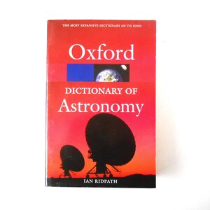 May include: A red book with the title "Oxford Dictionary of Astronomy" by Ian Ridpath. The cover features a silhouette of a radio telescope against a sunset sky.