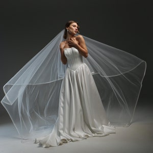 May include: A white wedding dress with a strapless bodice and a flowing skirt. The dress is paired with a long, white veil.
