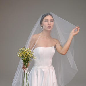 May include: A bride wearing a white strapless wedding dress with a long veil and holding a bouquet of yellow flowers.