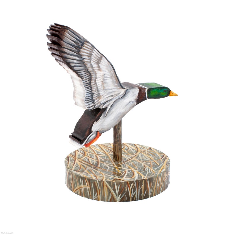 Op de afbeelding: Een houten eendenlokvogel met beschilderde details, geperst op een basis met een bruin en groen camouflagepatroon.