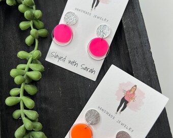 May include: Two pairs of handmade earrings with silver and pink or orange circles. The earrings are on a white card with the text "Handmade Jewelry" and "Slayed with Sarah".