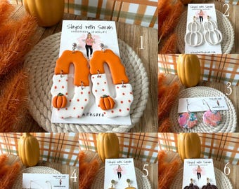 May include: Six pairs of dangle earrings on display cards labeled Slayed with Sarah. Designs include orange and white pumpkin patterns, floral prints, yellow sunflowers, and dark brown pumpkin motifs, all featuring various autumn-themed shapes.