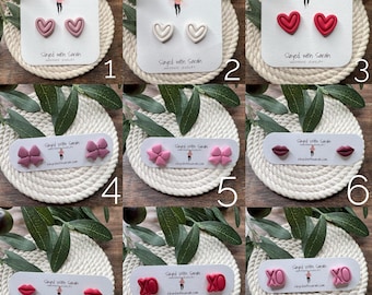 May include: Nine different pairs of polymer clay earrings in various shapes and colors, including hearts, bows, lips, and the letters XO. The earrings are displayed on white cards with the text "Slayed with Sarah" on each card.