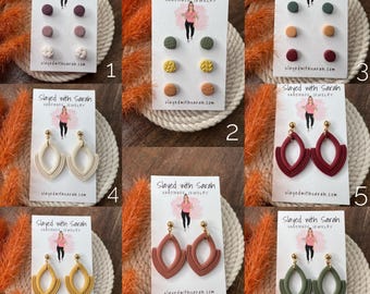 May include: A collection of handmade earrings and stud earrings in various colors and designs. The image includes stud earrings with textured patterns and teardrop-shaped dangle earrings. The brand name "Slayed with Sarah" is visible on the packaging.