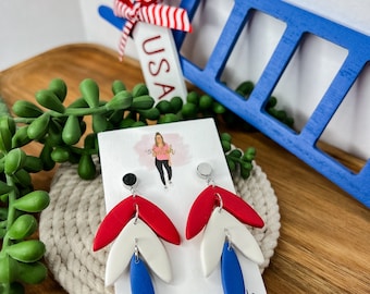 May include: Red, white, and blue dangle earrings with a layered design. The earrings are handmade and feature a silver hook.