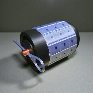 Może przedstawiać: Cylindryczny obiekt z czarną podstawą i jasnoniebieską sekcją w kształcie siatki. Siatka ma małe, ciemnofioletowe kropki. Jasnoniebieska pętla i miedziany pierścień są przymocowane z boku.