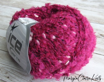 May include: A ball of vibrant fuchsia yarn with white and black flecks. The yarn has a textured, fuzzy appearance. A label from ICE Yarns is partially visible, along with the text "Maryia Claire Knits".