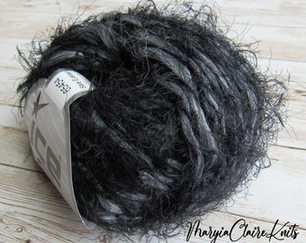 May include: A ball of black and gray yarn with a fuzzy texture. The yarn has a label with the number 65454 and the brand name "ICE". The yarn is likely used for knitting or crocheting projects.